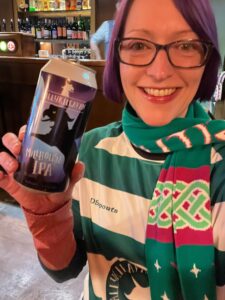 Pale white lady in St Brigid's Day scarf with a can of Ballykilcavan Millhouse IPA at Juno